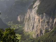 The view stretches across steep rock faces and green valley slopes deep into the Lauterbrunnen Valley. In the background, rugged mountain peaks such as the Breithorn and glaciers rise up, some of them shrouded in clouds.