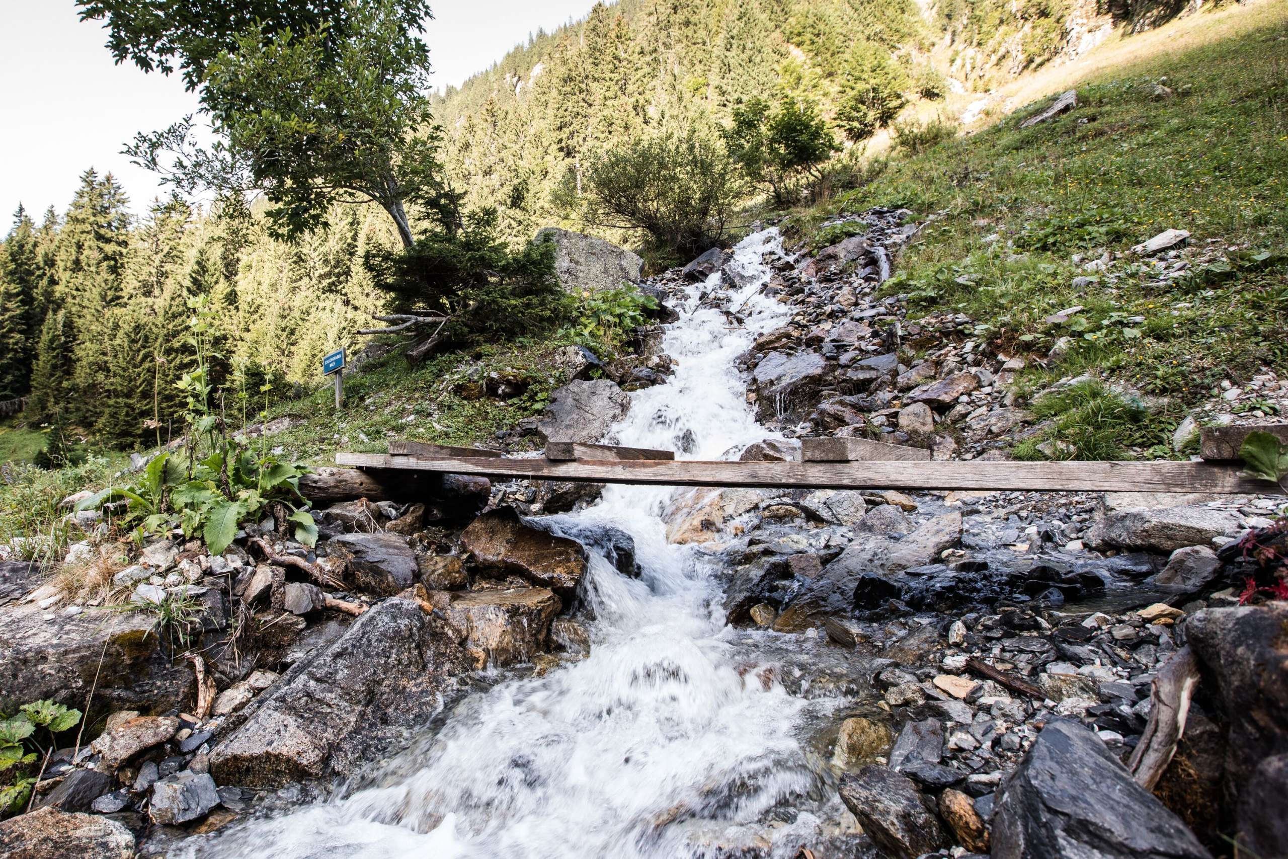 The mountain stream flows unstoppably. A small bridge leads over the stream into the rear Lauterbrunnen valley.