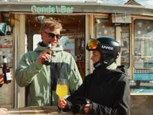 Three people raise their glasses together at the Gondelbar near the Hotel Jungfrau in Mürren. The cozy terrace, with its view of the snow-covered mountain landscape, is the perfect place to relax after a day on the slopes.