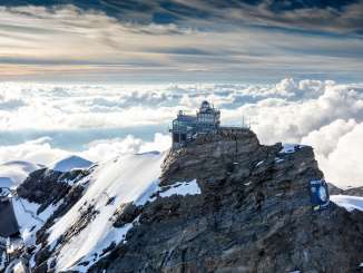 A bird's-eye view of the Jungfraujoch, surrounded by snow, with a sea of fog in the background.