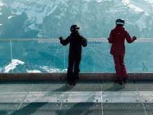 Deux femmes en tenue de ski se tiennent près de la balustrade de la plate-forme Skyline Walk et admirent la vue sur l'Eiger, le Mönch et la Jungfrau.