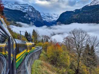 The Wengernalpbahn runs along the mountainside above the Lauterbrunnen Valley. Fog hangs over the valley, while forests and steep cliffs line the route.