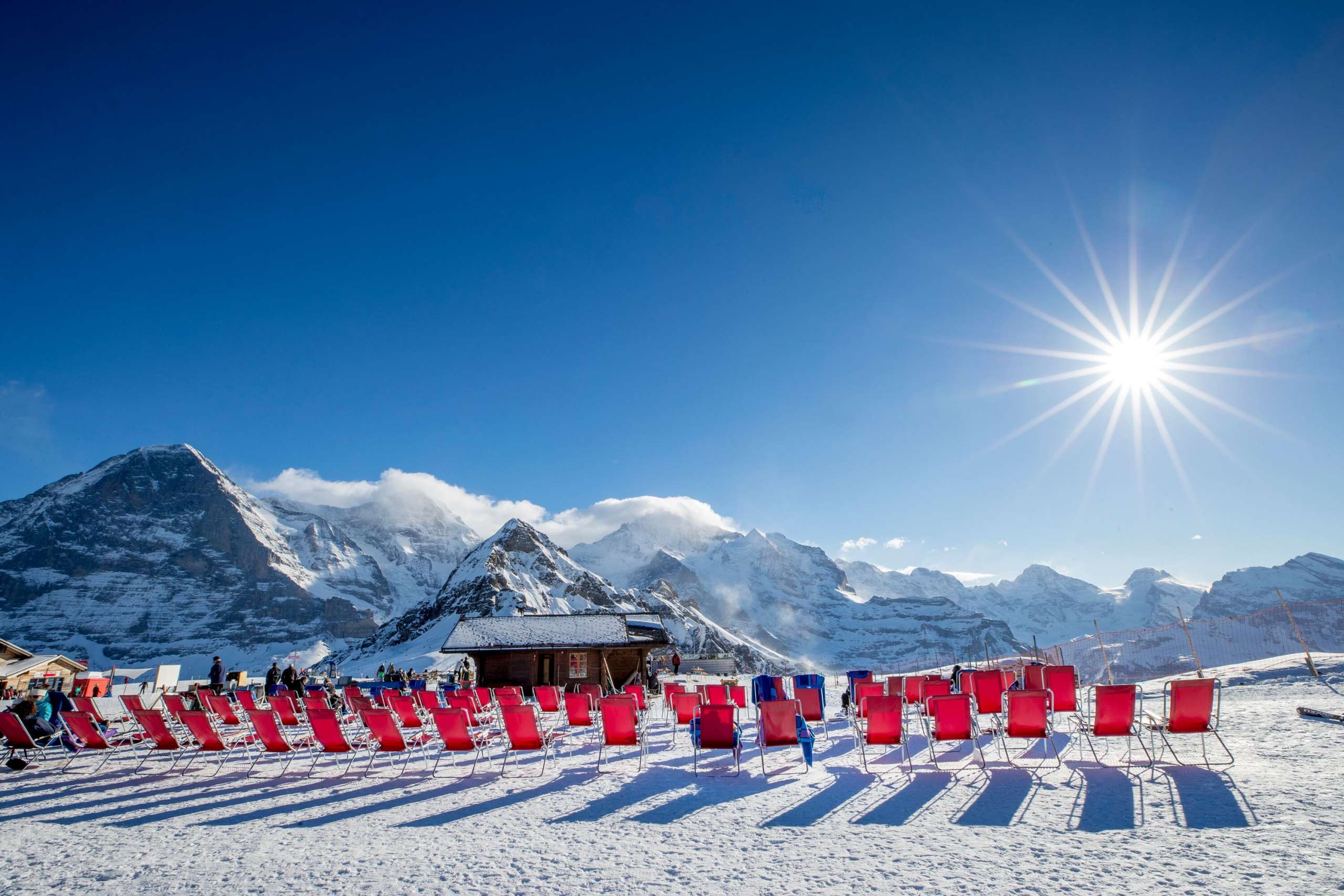 Les chaises rouges sont bien alignées au soleil pour les skieurs fatigués. La vue sur l'Eiger, le Mönch et la Jungfrau offre un magnifique panorama hivernal.