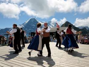 At the Mountain Spring Festival on the Männlichen, people dance in front of the panoramic view of the Eiger. The dancers are dressed in traditional costumes.