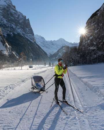 A cross-country skier pushing a stroller on the trail in Lauterbrunnen.