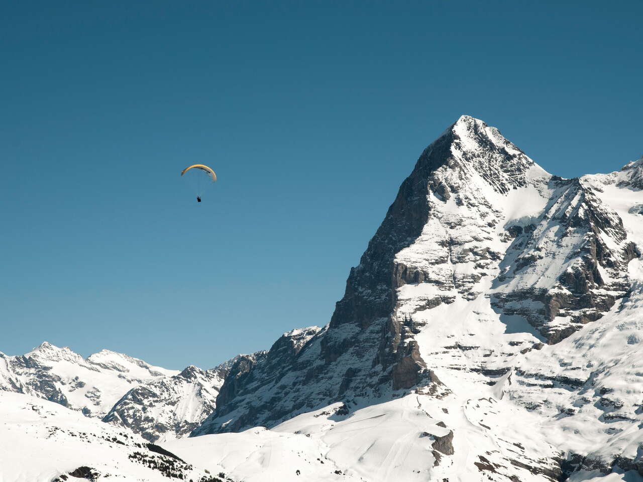 Winterlicher Paragliding Flug mit Sicht auf den verschneiten Eiger und die kleine Scheidegg.