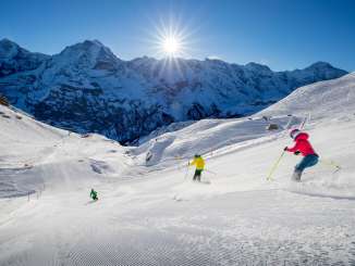 Skiers carve turns in the Mürren-Schilthorn ski area. The trio of the Eiger, Mönch, and Jungfrau can be seen in the distance.