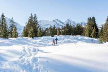 Hiking on snowshoes through the snow-covered landscape on a sunny day. The snowshoe trail in Mürren offers a unique view of the Gspaltenhorn.