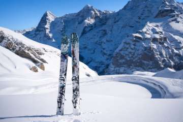Two skiers in deep snow against a snow-covered mountain backdrop