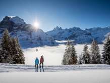 Winter hike on snow-covered trails around Grindelwald. Hikers enjoy the sunny day and the breathtaking view of the Eiger.