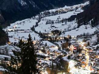 The Lauterbrunnen Valley opens up between steep rock faces, while the lights of the village shine in the valley floor. The wintry mountain landscape appears serene and majestic beneath the dark sky.