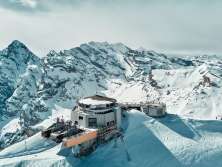Die Drohnenaufnahme zeigt das Schilthorn mit dem markanten Drehrestaurant Piz Gloria und der Bergstation, eingebettet in die verschneite Hochgebirgslandschaft. Rund um den Gipfel erstrecken sich die schneebedeckten Bergketten der Berner Alpen und verleihen der Szenerie ihre eindrucksvolle Weite.