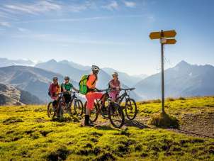 The cyclists look at the signpost and enjoy the view from Hasliberg. The view offers a summery panorama of the mountain landscape.