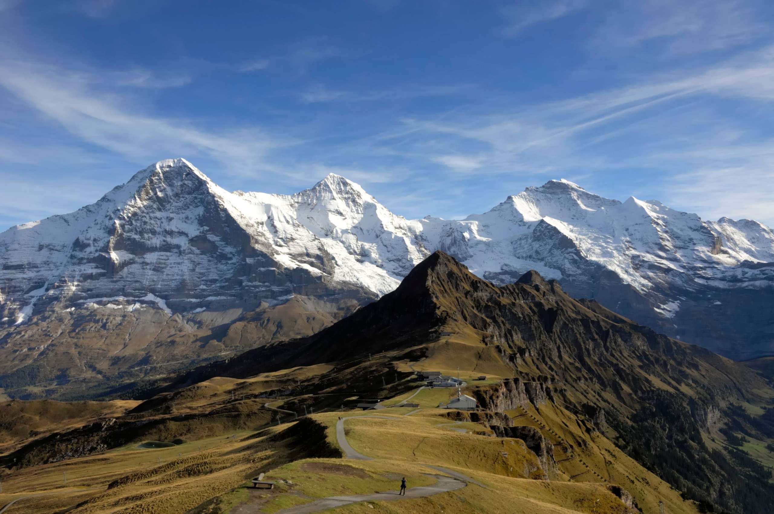 View of the summery Männlichen with the snow-covered triumvirate of the Eiger, Mönch and Jungfrau in the background.