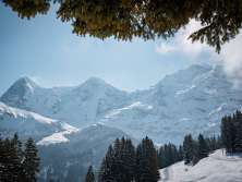 Vue d'en haut, on admire le paysage enneigé qui borde la ligne BLM entre Grütschalp et Mürren. La ligne ferroviaire traverse des pentes blanches, longeant ici et là des chalets isolés et des sapins, avec une vue imprenable sur les sommets environnants.