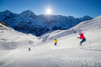 Skiers carve turns in the Mürren-Schilthorn ski area. The trio of the Eiger, Mönch, and Jungfrau can be seen in the distance.