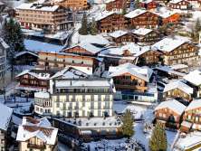Luftaufnahme des Bergdorfs Wengen mit verschneiten Chalets, Hotels und Strassen. Das Dorf liegt eingebettet am Hang unterhalb eines winterlichen Waldgebiets.